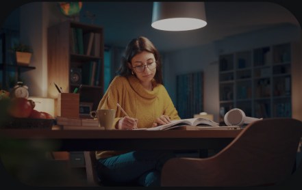 A woman writing at a desk under a warm lamp.
