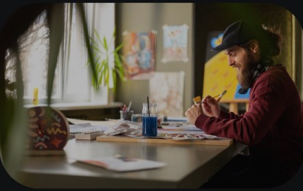 A man painting at a sunlit desk.