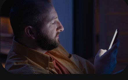 A man looking at a phone screen in a dark room.